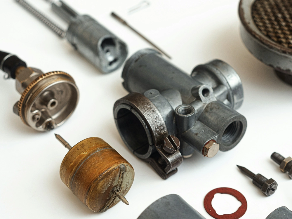 Various parts and tools for assembling a gas engine, including pistons, spark plugs, and wrenches on a workbench.
